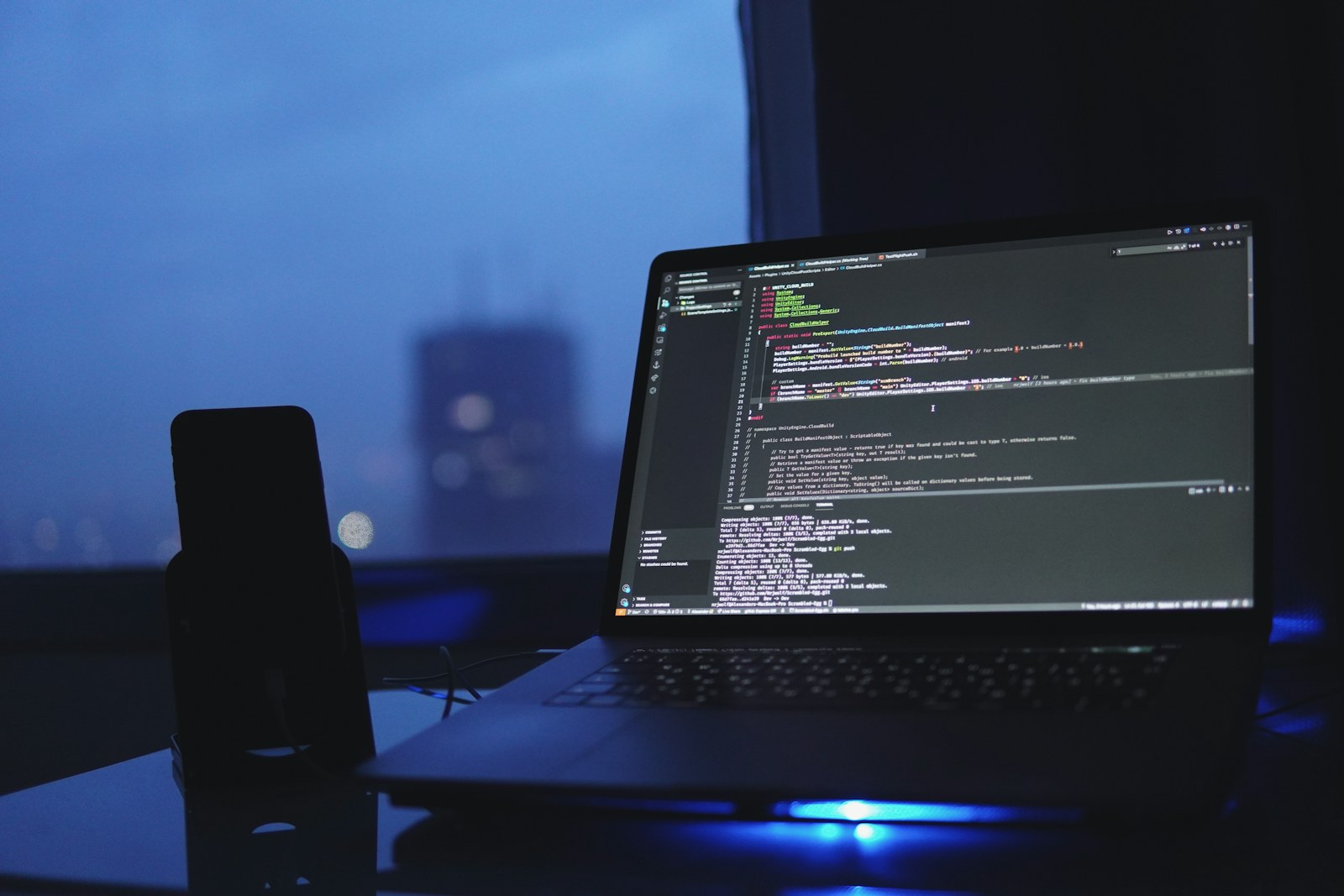 A laptop displaying code on a blue-lit desk.